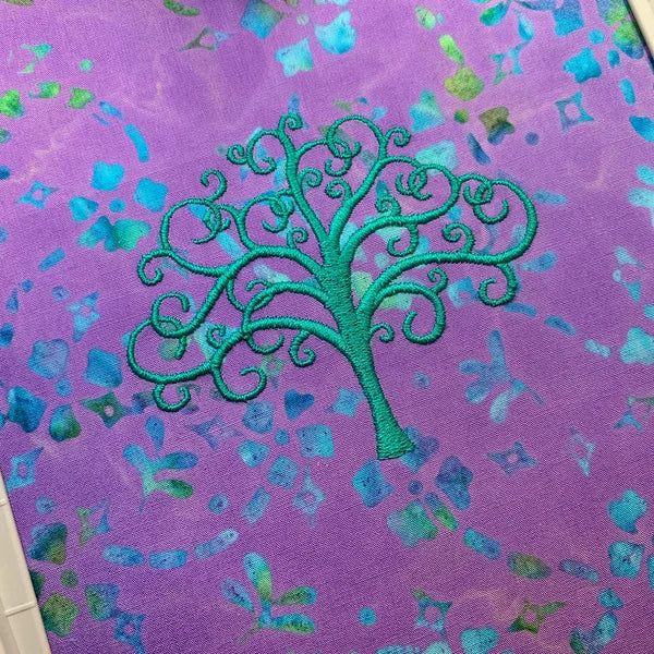 Tree Of Life Machine Embroidery stitch-out: Embroidered green tree design on a purple fabric with blue and green shapes