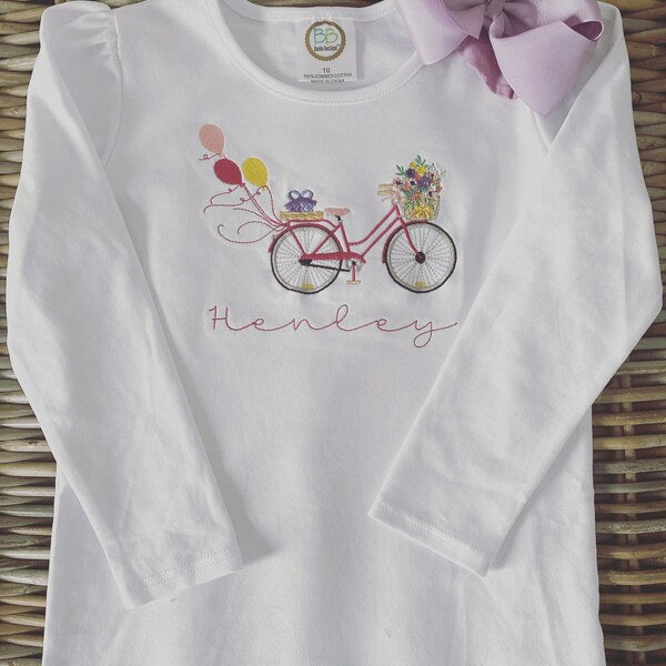 Bicycle With Flowers Machine Embroidery Design stitch-out: White long-sleeve shirt with bicycle and balloon design on a woven surface