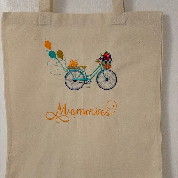 Bicycle With Flowers Machine Embroidery Design stitch-out: Beige tote bag with bicycle and flowers design and 'Memories' text on a white