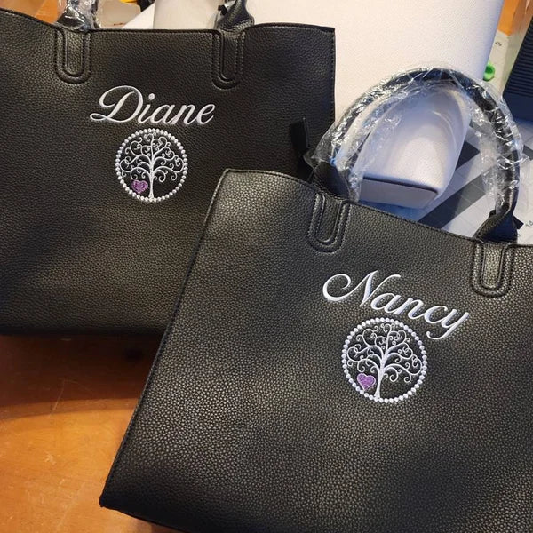 Tree Of Life Machine Embroidery stitch-out: Two black bags with personalized names 'Diane' and 'Nancy' on a wooden surface.