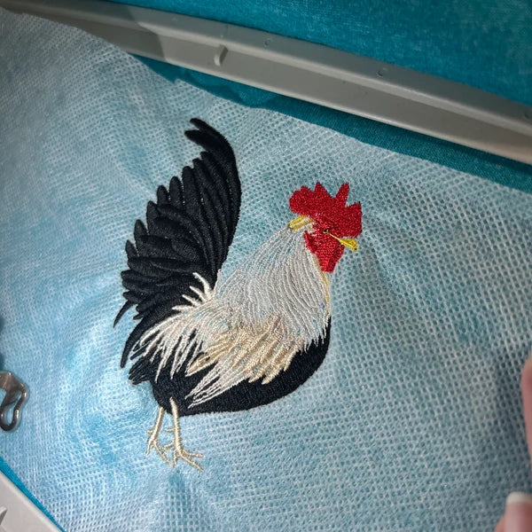 Golden Rooster Embroidery Design stitch-out: Embroidery of a rooster on a blue fabric with a hoop.