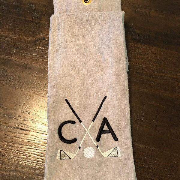 Golf Club Embroidery design stitch-out: Beige towel with 'CA' and crossed golf clubs design on a wooden surface