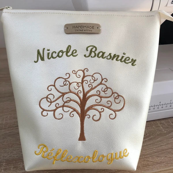 Tree Of Life Machine Embroidery stitch-out: White pouch with embroidered tree design and text on a wooden surface