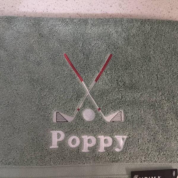Golf Club Embroidery design stitch-out: Gray towel with embroidered golf clubs and 'Poppy' text on a white background