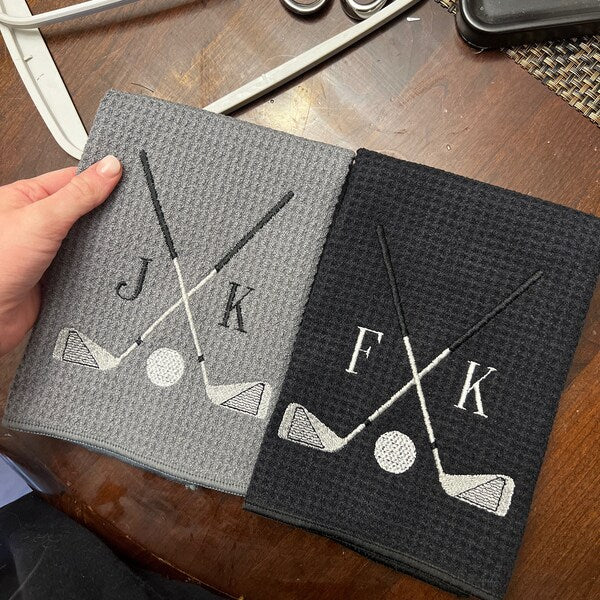 Golf Club Embroidery design stitch-out: Two embroidered towels with golf designs and initials on a wooden surface.