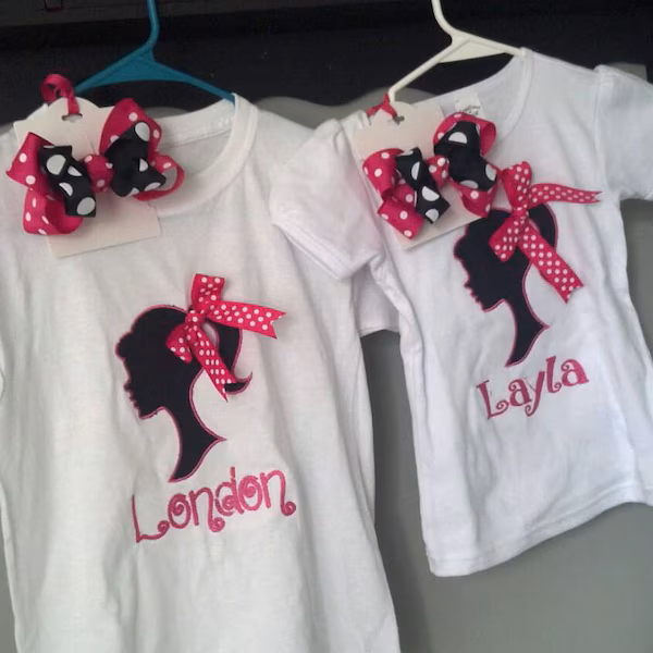 Girl Princess Head Silhouette stitch-out: Two white shirts with black silhouette designs, red bows, and names 'London' and 'Layla'