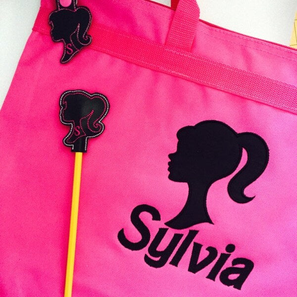 Girl Princess Head Silhouette stitch-out: Pink apron with black silhouette of a princess and the name 'Sylvia' on a